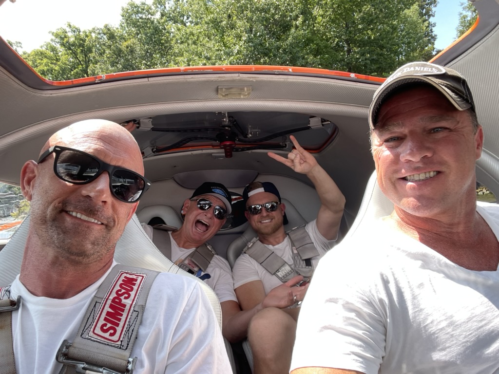 Four friends grinning in racing harnesses inside a car
